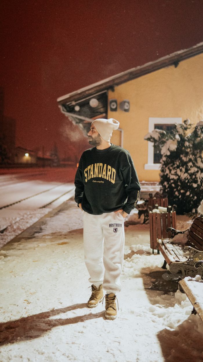 A bearded man in winter attire walking on a snow-covered street at night.