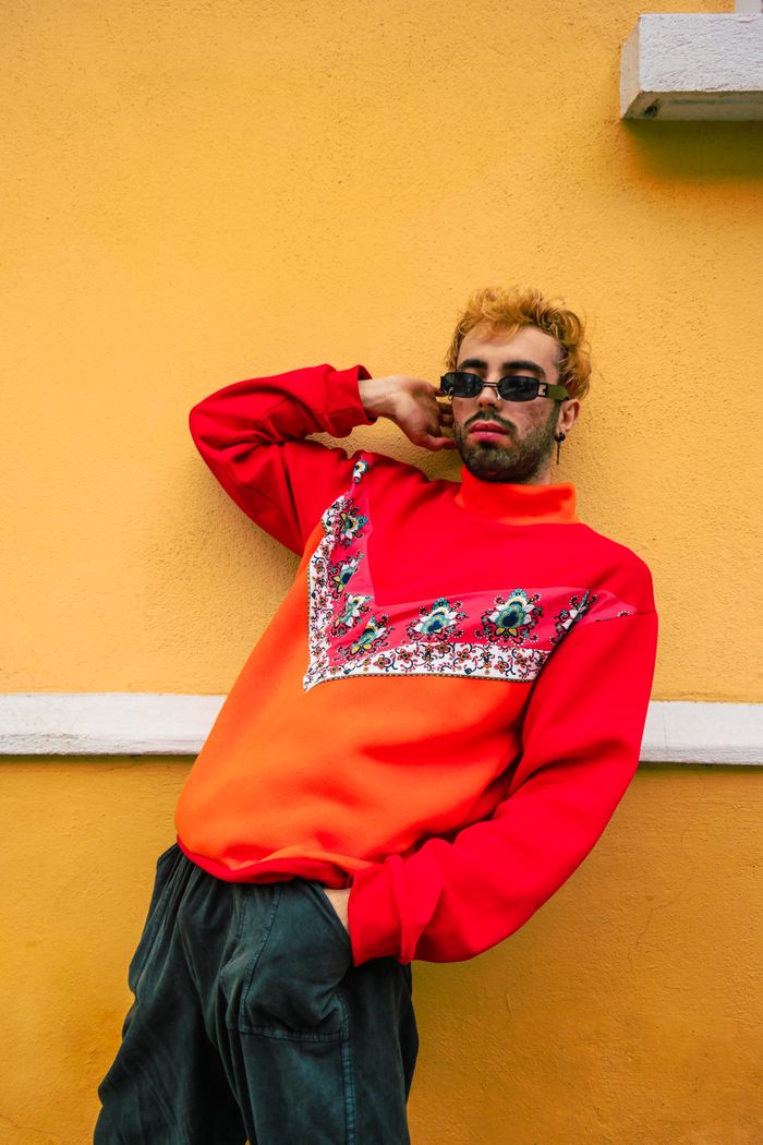 Fashionable male model in vibrant red sweatshirt posing confidently against a bright orange wall.