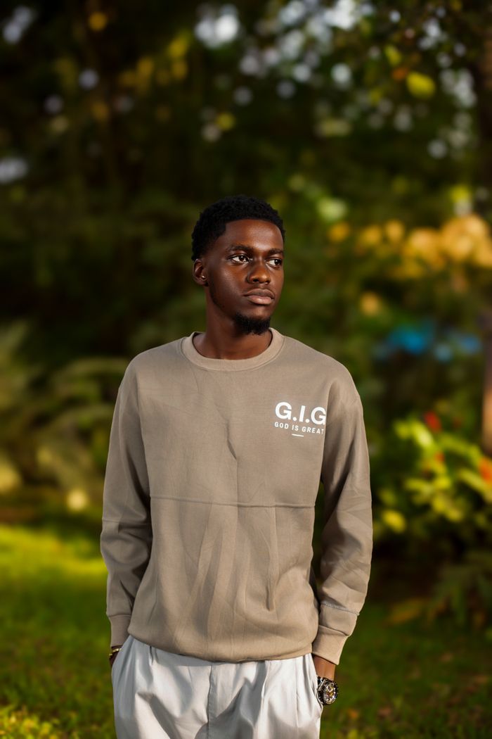 Portrait of a young man standing confidently outdoors in a lush green setting.