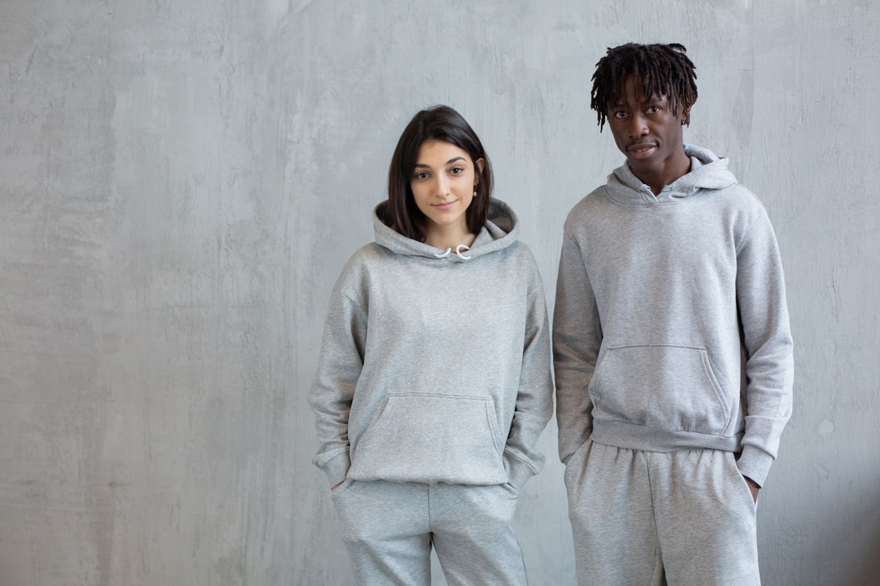 Smiling diverse man and woman wearing similar sports suits standing with hands in pockets and looking at camera